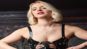 Goddess Sandra en lingerie noire avec une posture dominante assise sur un lit