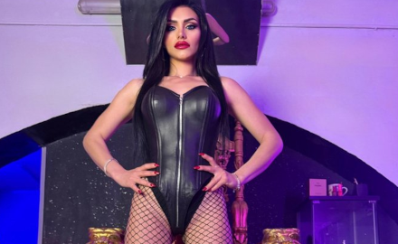 Mistress Iside en tenue noire avec une posture dominante devant un décor royal