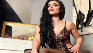 Mistress Iside en tenue noire avec une présence dominante et un décor stylisé